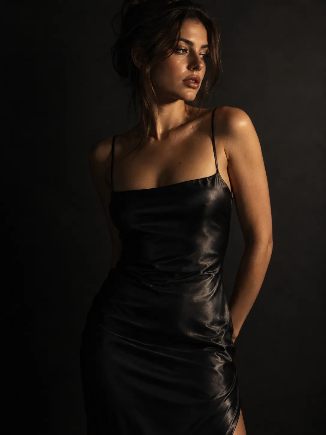 Adult woman in a black satin slip dress under one hard key light on a dark backdrop